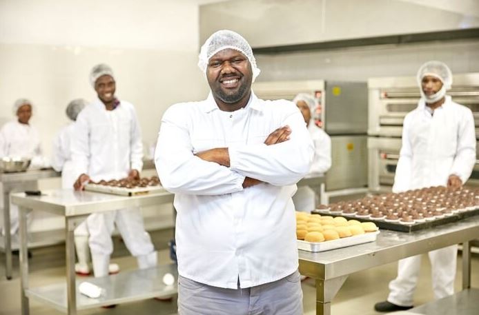 Head baker and leader of a bakery stands with arms folded with smile on face.