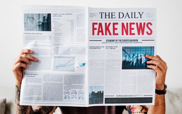 Man reading a newspaper with the words "Fake News" written on the front page in red.