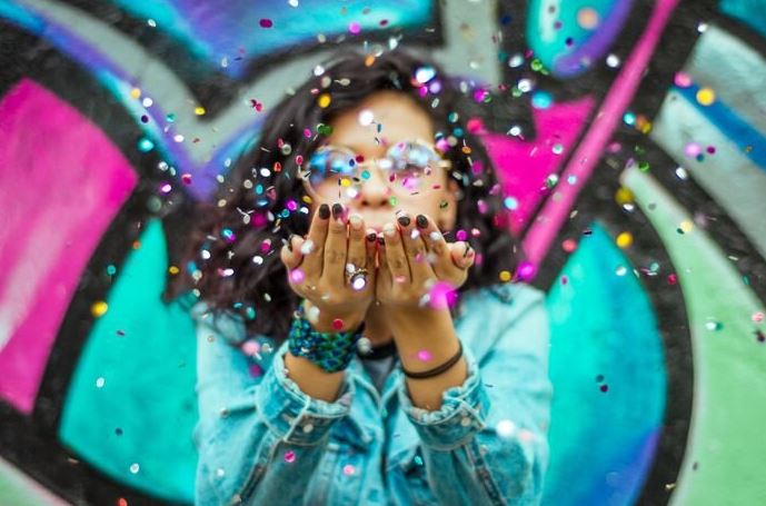 Women business owner blowing small colorful pieces of confetti off her hands.