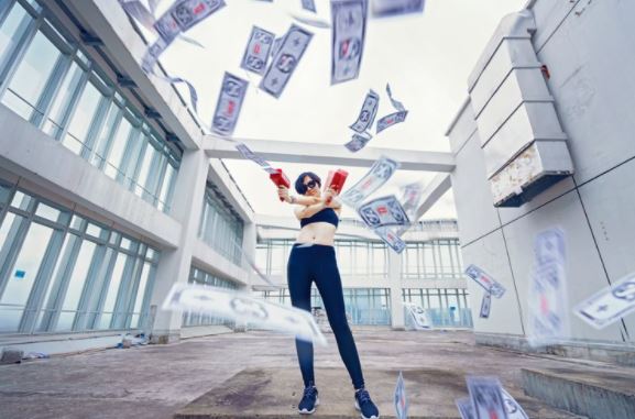 White lady standing in a court yard surrounded by buildings firing money into the air.