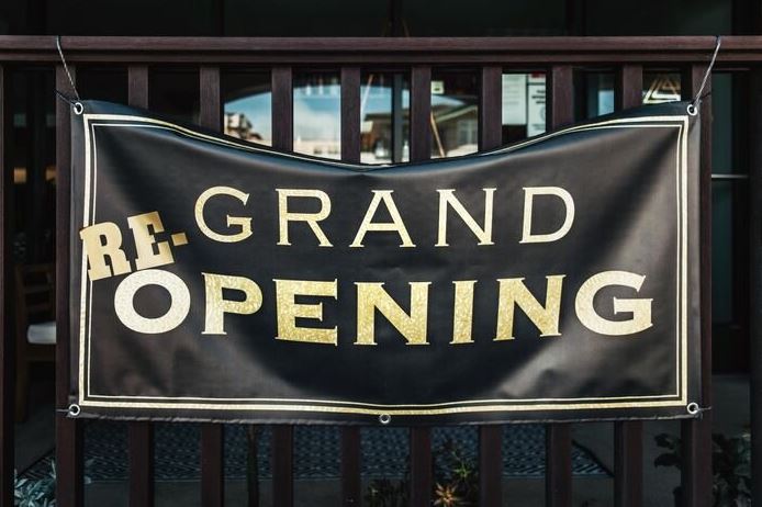 A black banner in front of a store with the words "Grand re opening" on it.