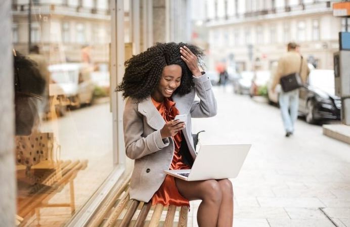 Black women sitting on a bench outside busy shopping online.