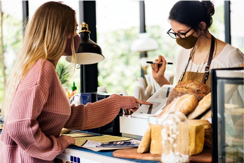 Female customer pointing to a till while the business owner helps with telling up the items that the lady bought.