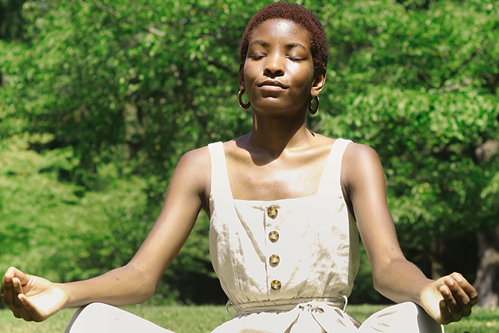 Black women dealing with anxiety by meditating in an outdoor environment.