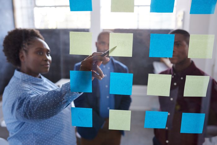 Black women writing on sticky notes about combining the principles of circular economy with food design and two colleagues in the background give their input.